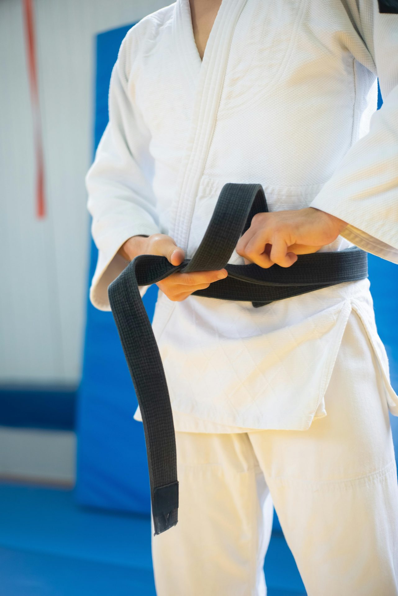 Close-up of a judoka in white uniform tying a black belt, indicating discipline and skill.