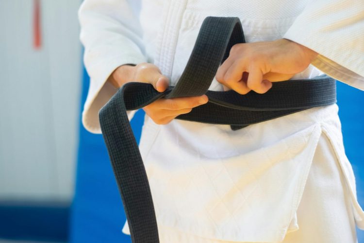Close-up of a judoka in white uniform tying a black belt, indicating discipline and skill.